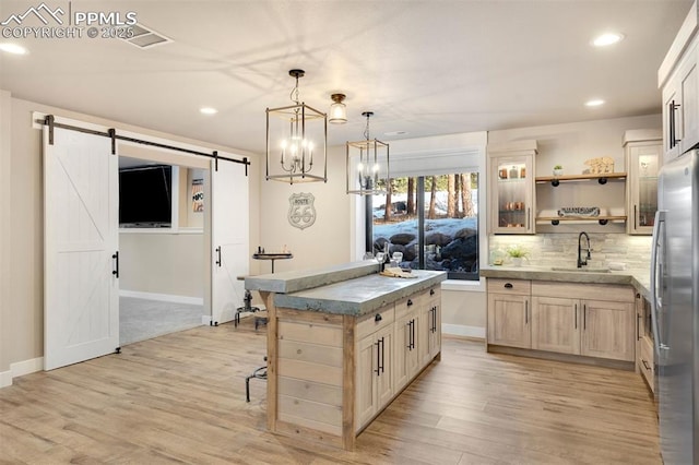 kitchen with sink, a center island, light brown cabinets, stainless steel refrigerator, and a barn door