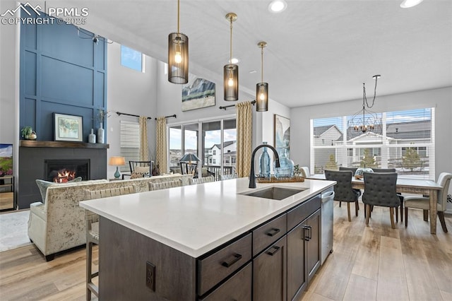 kitchen with sink, dishwasher, a kitchen island with sink, dark brown cabinetry, and a large fireplace