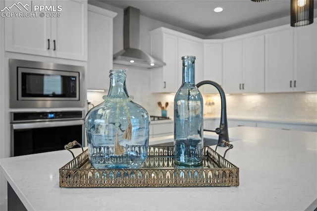 room details with white cabinets, a kitchen island, wall chimney exhaust hood, and appliances with stainless steel finishes