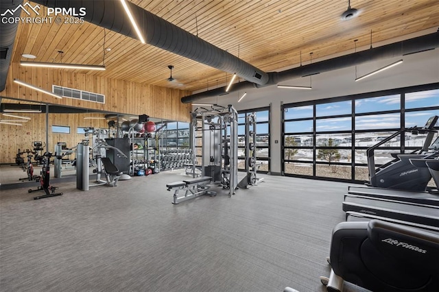 workout area with wooden ceiling, a high ceiling, and wood walls