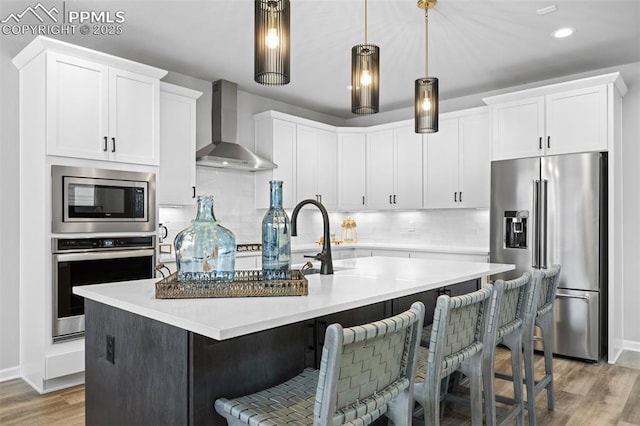 kitchen featuring decorative light fixtures, an island with sink, wall chimney exhaust hood, and appliances with stainless steel finishes