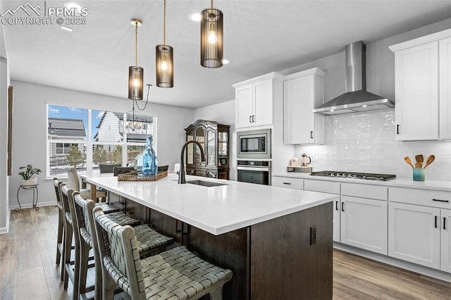 kitchen with pendant lighting, wall chimney range hood, sink, white cabinetry, and stainless steel appliances