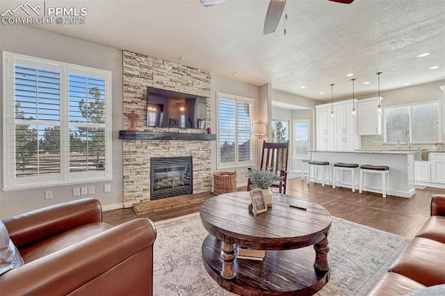 living room featuring ceiling fan, a stone fireplace, wood-type flooring, and a textured ceiling