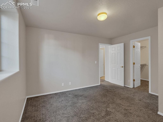 unfurnished bedroom with a walk in closet, a closet, and dark colored carpet