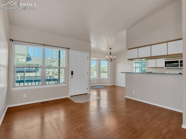 unfurnished living room featuring lofted ceiling, dark wood-type flooring, and an inviting chandelier