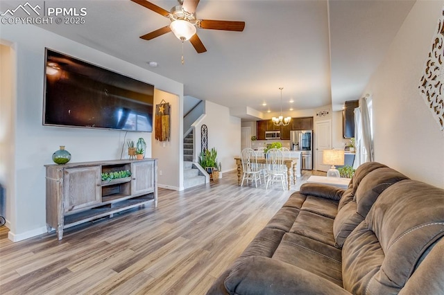 living room with ceiling fan with notable chandelier and light hardwood / wood-style flooring