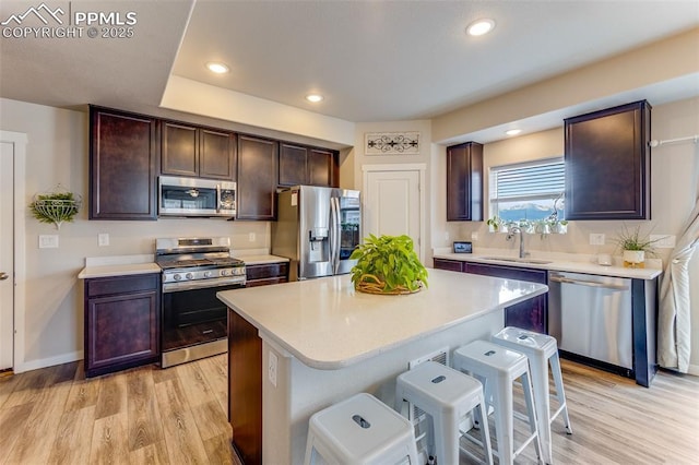 kitchen featuring a breakfast bar area, a center island, dark brown cabinets, appliances with stainless steel finishes, and light hardwood / wood-style floors