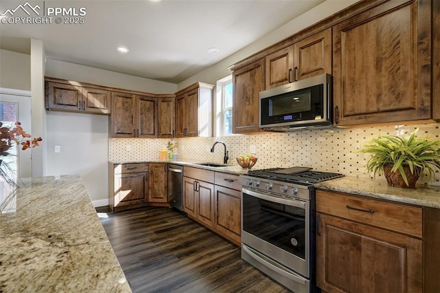 kitchen featuring sink, light stone counters, dark hardwood / wood-style floors, stainless steel appliances, and decorative backsplash