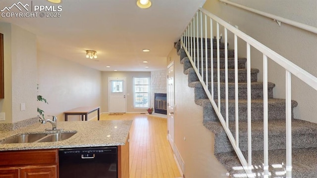 kitchen with sink, light wood-type flooring, black dishwasher, a fireplace, and light stone countertops