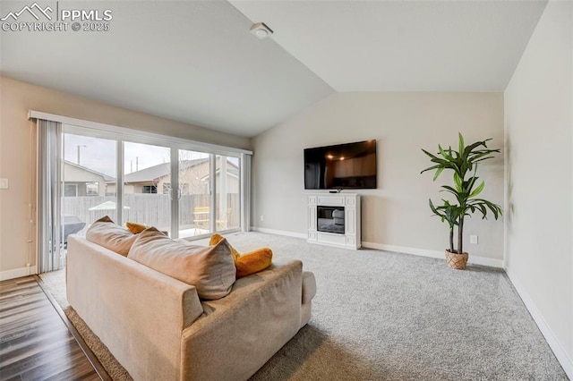 living area featuring lofted ceiling, carpet, a glass covered fireplace, and baseboards