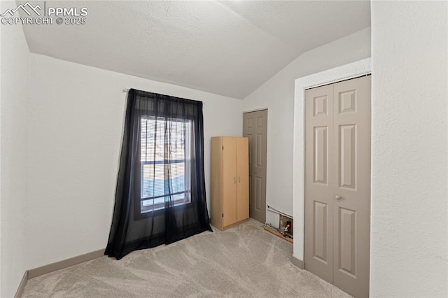 unfurnished bedroom with light carpet, vaulted ceiling, and a textured ceiling