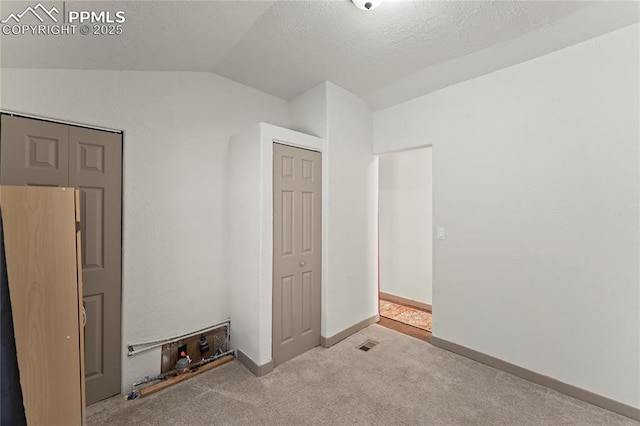 unfurnished bedroom with lofted ceiling, light carpet, and a textured ceiling