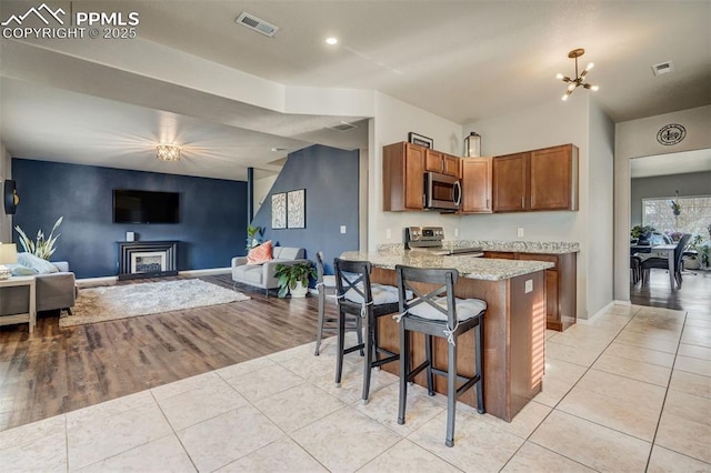 kitchen with light tile patterned flooring, a breakfast bar, a notable chandelier, kitchen peninsula, and stainless steel appliances