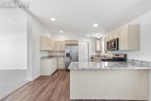 kitchen featuring lofted ceiling, sink, appliances with stainless steel finishes, kitchen peninsula, and cream cabinetry