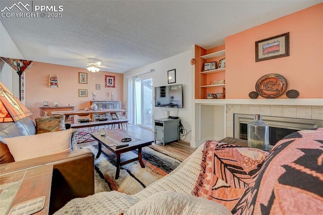 living room featuring a textured ceiling, light wood-type flooring, built in features, ceiling fan, and a fireplace