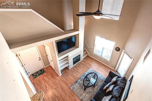 living room featuring hardwood / wood-style flooring, ceiling fan, a tile fireplace, and a towering ceiling