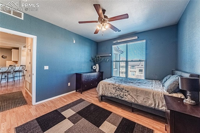 bedroom with ceiling fan, wood-type flooring, and a textured ceiling