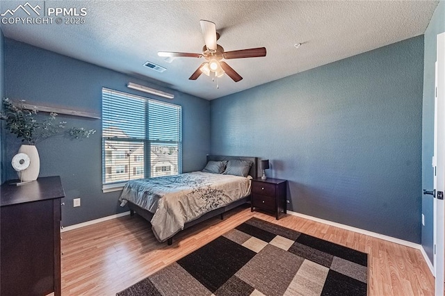 bedroom with a textured ceiling, wood-type flooring, and ceiling fan