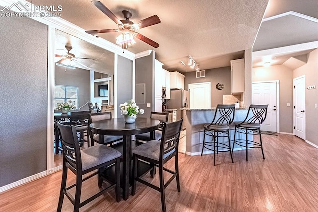 dining space featuring lofted ceiling, rail lighting, a textured ceiling, and light wood-type flooring