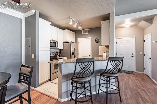 kitchen featuring white cabinetry, decorative backsplash, dark stone counters, light hardwood / wood-style floors, and stainless steel appliances