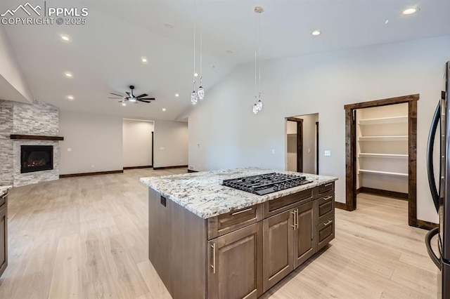 kitchen featuring refrigerator, hanging light fixtures, a kitchen island, a stone fireplace, and stainless steel gas stovetop