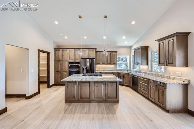 kitchen featuring sink, hanging light fixtures, a center island, stainless steel appliances, and light stone countertops