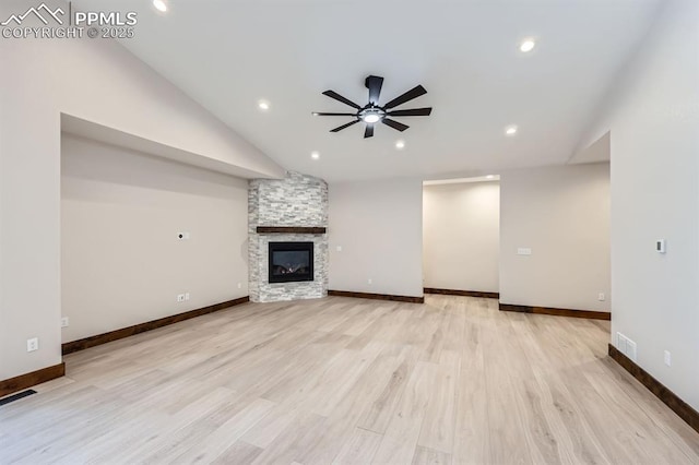 unfurnished living room with ceiling fan, lofted ceiling, a stone fireplace, and light hardwood / wood-style floors