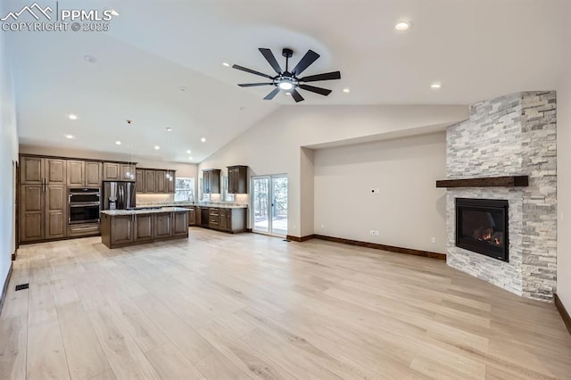 unfurnished living room featuring ceiling fan, high vaulted ceiling, a stone fireplace, and light hardwood / wood-style floors