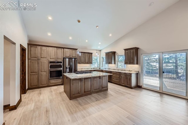 kitchen with pendant lighting, sink, appliances with stainless steel finishes, light stone counters, and a kitchen island