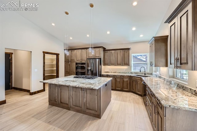 kitchen featuring sink, stainless steel appliances, a center island, light stone counters, and decorative light fixtures