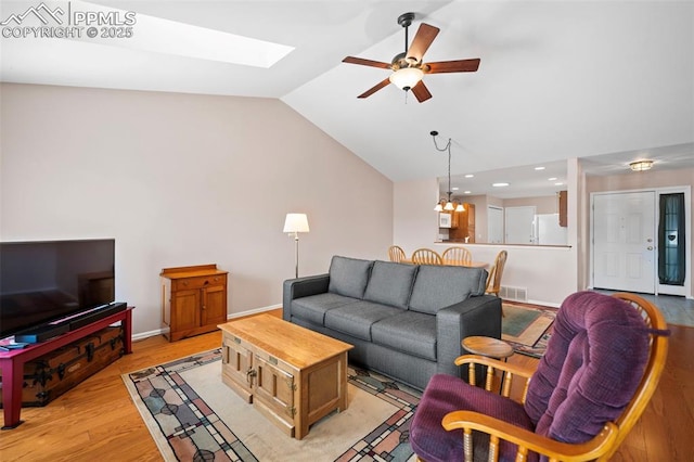 living room with ceiling fan with notable chandelier, lofted ceiling with skylight, and light hardwood / wood-style flooring