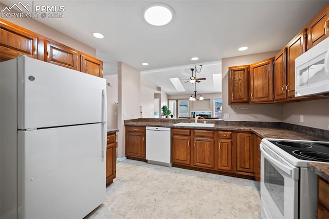 kitchen featuring white appliances, sink, lofted ceiling with skylight, and decorative light fixtures