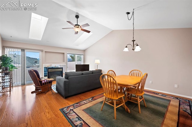 dining space with ceiling fan with notable chandelier, light wood-type flooring, and vaulted ceiling with skylight