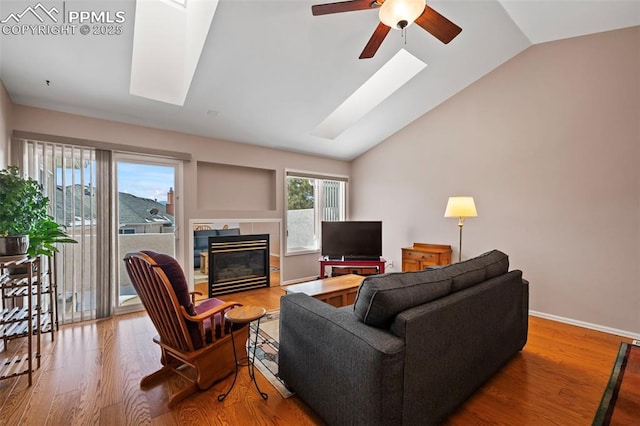 living room with a tile fireplace, vaulted ceiling with skylight, wood-type flooring, and ceiling fan