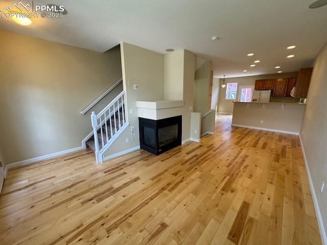 unfurnished living room featuring a multi sided fireplace and light hardwood / wood-style flooring