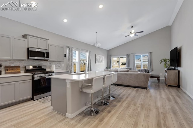 kitchen with appliances with stainless steel finishes, a breakfast bar area, gray cabinetry, a kitchen island with sink, and light hardwood / wood-style floors