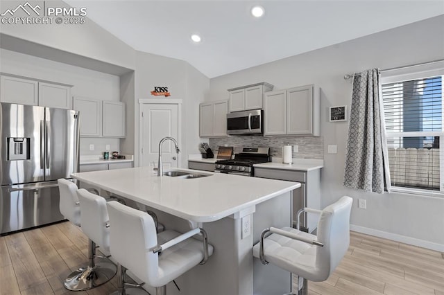 kitchen featuring sink, gray cabinetry, stainless steel appliances, a kitchen breakfast bar, and an island with sink