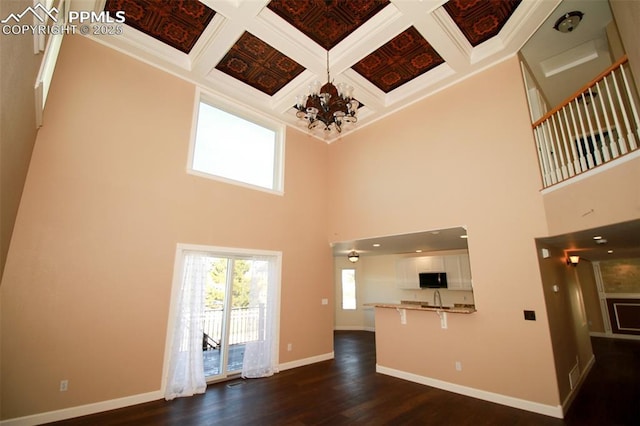 unfurnished living room featuring coffered ceiling, dark hardwood / wood-style floors, a high ceiling, and a notable chandelier