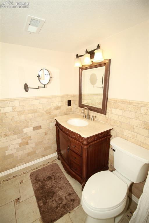 bathroom featuring vanity, toilet, and tile walls