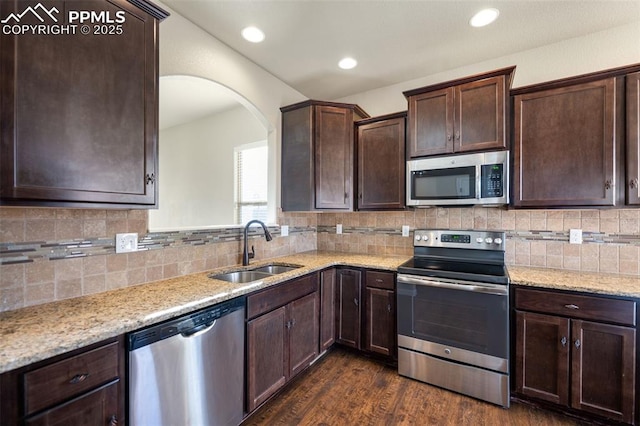 kitchen featuring dark hardwood / wood-style floors, sink, backsplash, stainless steel appliances, and light stone countertops