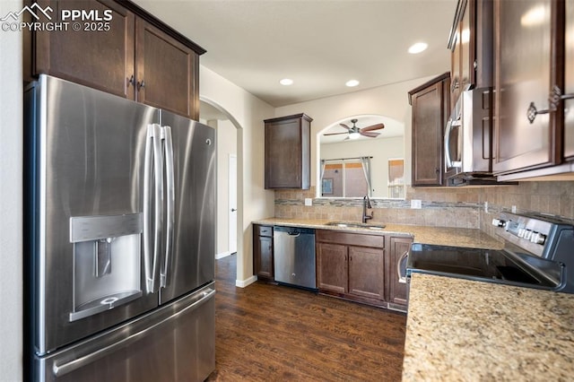 kitchen featuring dark wood-type flooring, sink, light stone counters, stainless steel appliances, and decorative backsplash