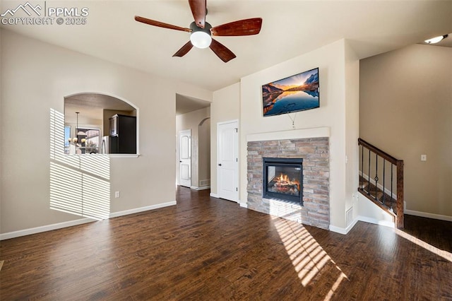 unfurnished living room with dark wood-type flooring, ceiling fan, and a stone fireplace