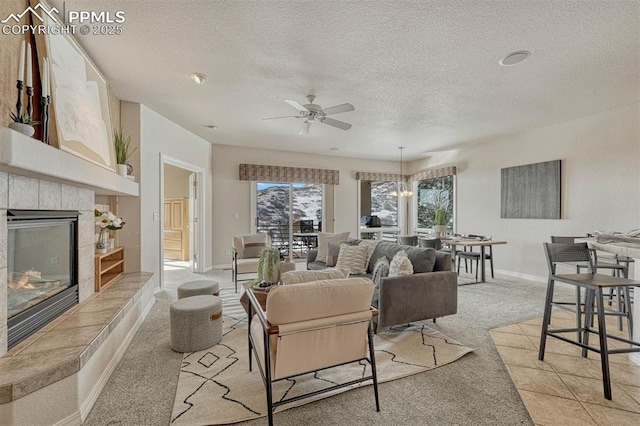 living room with a tiled fireplace, ceiling fan with notable chandelier, light carpet, and a textured ceiling