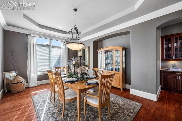 dining room with crown molding, a tray ceiling, and dark wood-type flooring