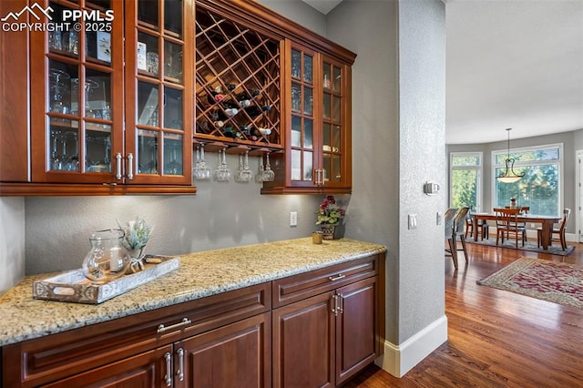 bar featuring pendant lighting, wood-type flooring, and light stone counters