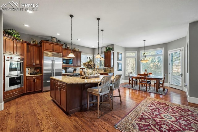 kitchen with pendant lighting, a breakfast bar area, built in appliances, light stone counters, and a kitchen island