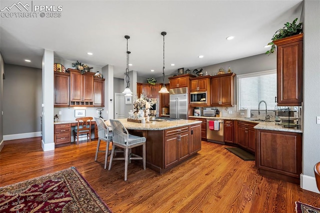 kitchen with sink, a breakfast bar area, a center island, built in appliances, and light stone counters