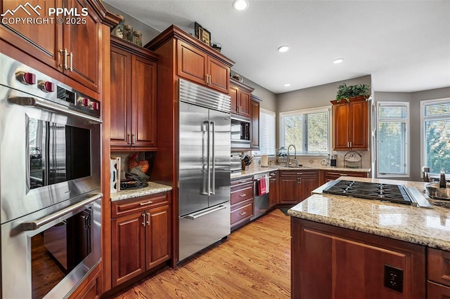 kitchen with light stone counters, built in appliances, sink, and light hardwood / wood-style flooring