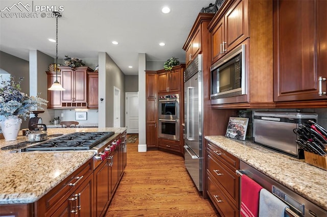 kitchen featuring hanging light fixtures, light stone countertops, built in appliances, and light hardwood / wood-style flooring