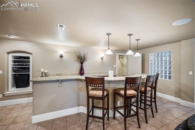 kitchen with pendant lighting, a kitchen breakfast bar, light stone countertops, and light tile patterned floors